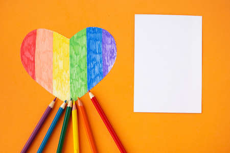 Heart in lgbtq colors, white mockup blank and pencils on bright orange background, top view, copy spaceの写真素材