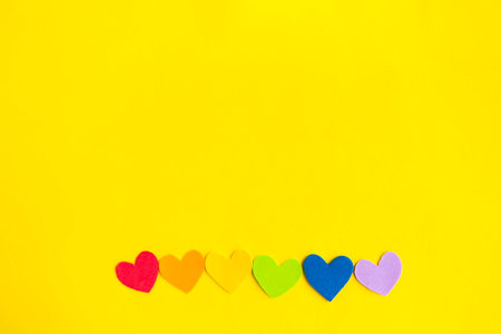 Hearts in lgbtq colors on bright yellow background, top view, copy space