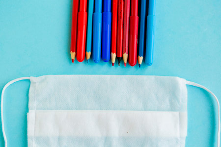 Color pencils and medical mask on blue background, top view, back to school concept, school...
