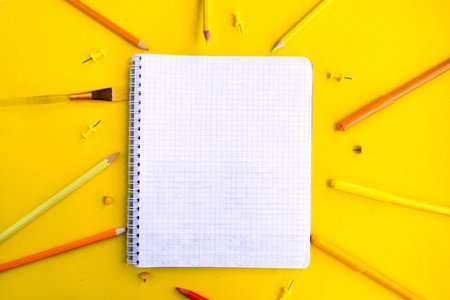 Color pencils and white mockup notebook on yellow background, top view