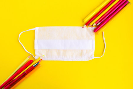 Color pencils and medical mask on bright yellow background. Back to school concept. School...
