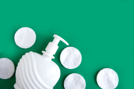 Cotton sponges and cosmetic bottle on dark green background, top view, copy space for the text