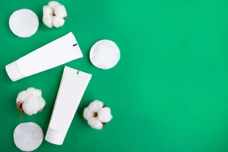 Cotton sponges and cosmetic bottles on dark green background, top view, copy space for the textの写真素材