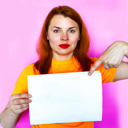 Redhead girl is holding white mockup blank on pink backgroundの写真素材