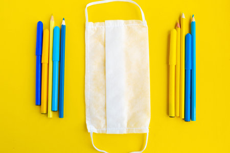 Color pencils and medical mask on yellow background, top view. Back to school concept. School...