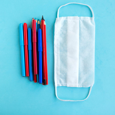 Color pencils and medical mask on blue background, top view. Back to school concept, school...