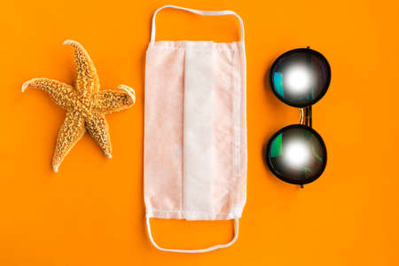 Starfish, medical mask and sunglasses on orange background. Coronavirus travel conceptの写真素材