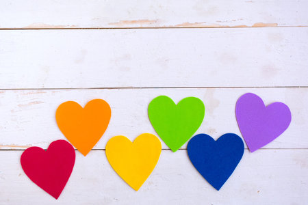 Hearts in lgbtq colors on wooden background, top view