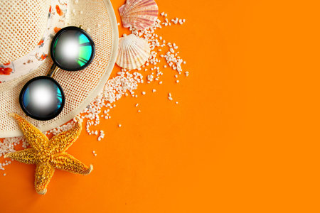 Straw hat, sunglasses and seashells on bright orange background. Summer vacation concept, copy space...