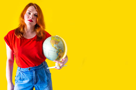 Portrait of beautiful redhead girl with globe on yellow background, travel concept