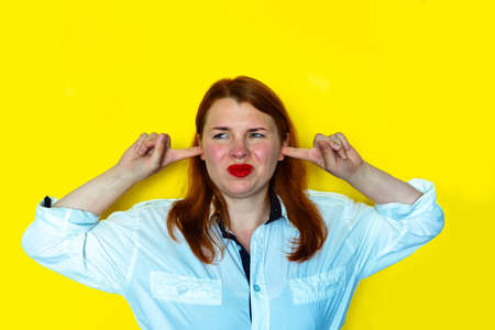 Portrait of redhead girl covers his ears, yellow backgroundの写真素材