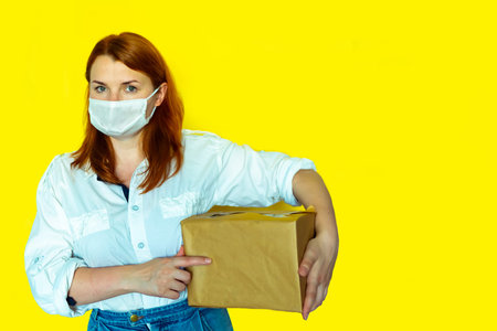 Food delivery girl in mask holds box in her hand yellow background coronavirus concept