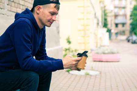 Young man sitting on a wooden bench in the park and drinking coffeeの写真素材