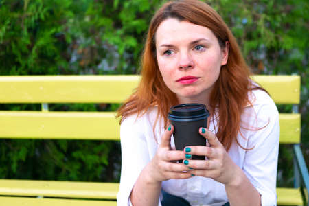 Thoughtful woman with coffee cup sits in the park, close upの写真素材