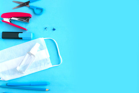 School supplies and medical mask on blue background, top view, copy space. Back to school concept