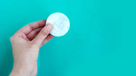 Woman hand holds cotton sponge on blue background, copy space for the text, minimal conceptの写真素材