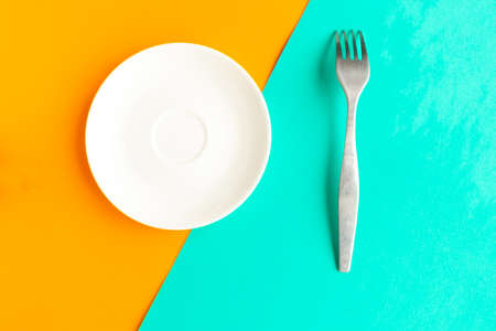 Empty plate and fork on orange and green geometric background. Copy space for the text. Minimal conceptの写真素材