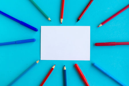 Color pencils and white mockup blank on blue background, top view