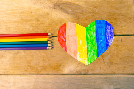 Pencils in lgbtq colors and heart on wooden background, top view