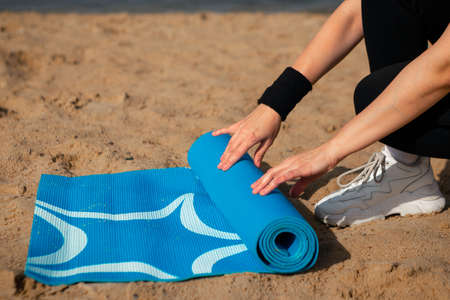 Exercise equipment, Woman's hands rolling yoga mat on the sea beach, outdoor sport conceptの写真素材