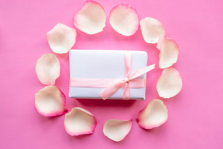 Gift box and rose petals on pink background, top viewの写真素材