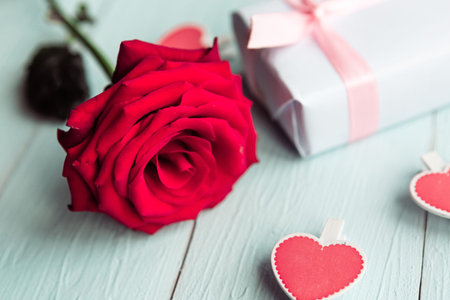 Red rose and gift box on wooden table, top view