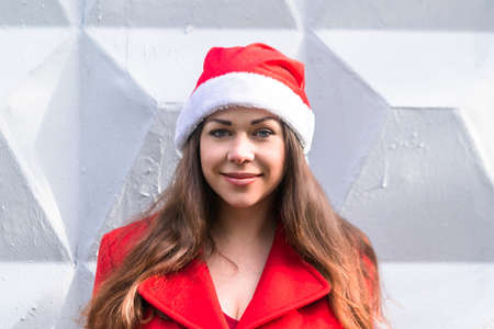 Portrait of beautiful brunette girl in Santa costume, white brick wall background. Merry Christmas and Happy New Yearの写真素材