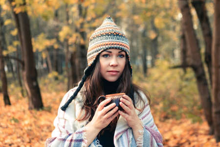 Portrait of young beautiful woman with coffee cup in autumn park, fall backgroundの写真素材