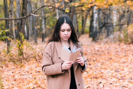 Beautiful woman read book in autumn park, fall backgroundの写真素材