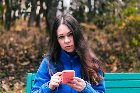 Beautiful woman with mobile phone in autumn park, fall background