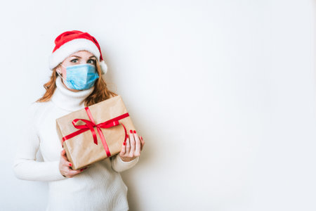 Portrait of woman in protective mask and Santa hat with gift box. Christmas with social distance. Coronavirus Christmas concept. Copy space for the textの写真素材