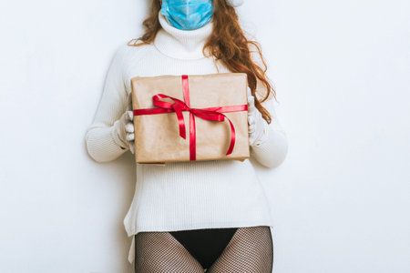Woman in face mask holding gift box with red ribbon. No face