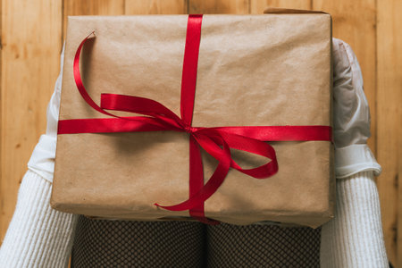 Human hands in white surgical gloves holding a gift box with red ribbon, top view.の写真素材