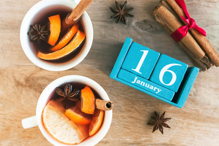 January 16. Blue cube calendar with month and date and cups with mulled wine, wooden background.