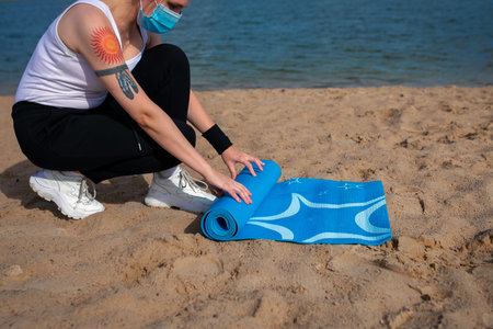 Minsk / Belarus - August 27 2020: Exercise equipment, Woman wearing face mask is rolling yoga mat on...