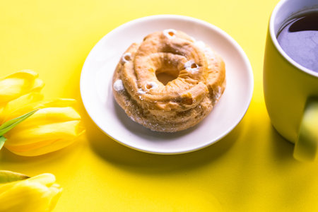 Bouquet of tulips, sweet donut and coffee cup on yellow background