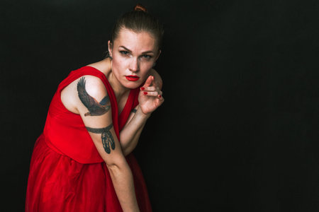 Fashion model in red beauty dress. Sexy woman with tattoos is posing in evening dress. Studio shot...