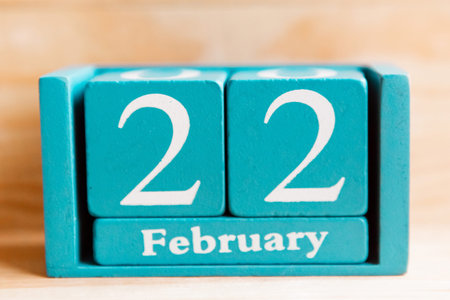 February 22. Blue cube calendar with month and date on wooden background.