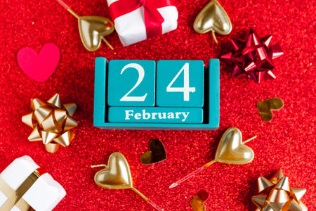 February 24. Blue cube calendar with month and date and decorations on red glitter background.