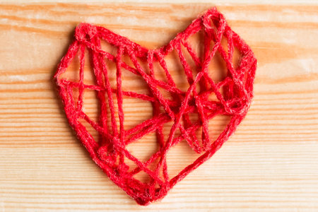 Valentine's Day Handmade Red Thread Heart on wooden background. Valentine's Day Holiday Background with hearts. Beautiful Hearts. Holiday of Love. Wedding conceptの写真素材