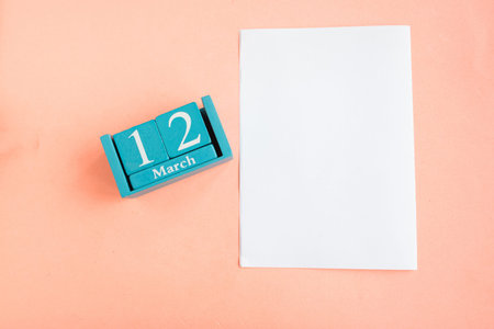 March 12. Blue cube calendar with month and date and white mockup blank on pink background.