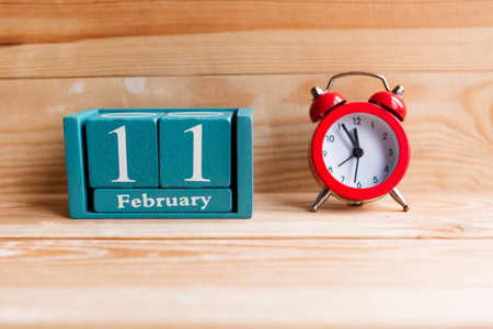 February 11. Blue cube calendar with month and date on wooden background.