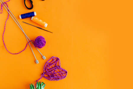 Purple thread handmade heart and needlework supplies on bright orange background. Copy space for the textの写真素材