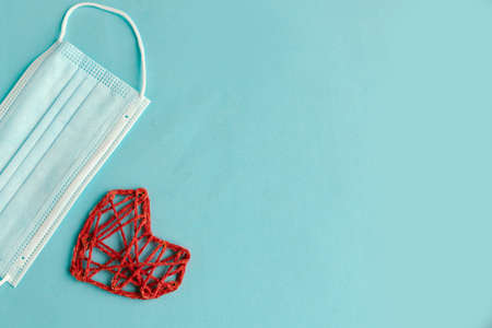 Red knitted craft heart and medical mask on blue background. Valentine's Day during the pandemic. Happy Valentine's Day 2021. Copy space gor the textの写真素材