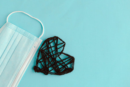 Black knitted heart and medical mask on blue background. Valentine's Day during the pandemic. Happy...