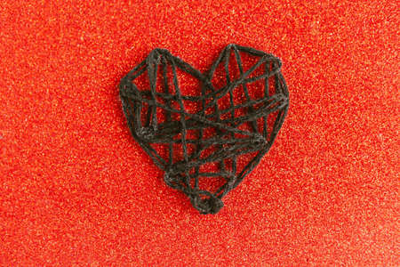 Black knitted handmade heart on red glitter background. Happy Valentine's Day.の写真素材