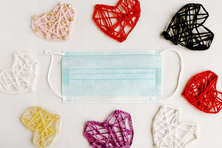 Knitted hearts and medical mask on white background. Valentine's Day during the coronavirus...