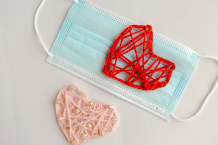 Two knitted hearts and medical mask on white background. Valentine's Day during the coronavirus...