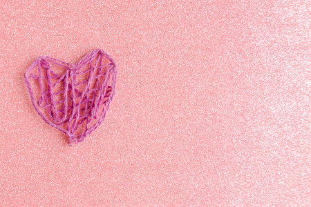 Purple knitted handmade heart on pink glitter background. Happy Valentine's Day. Copy space for the...