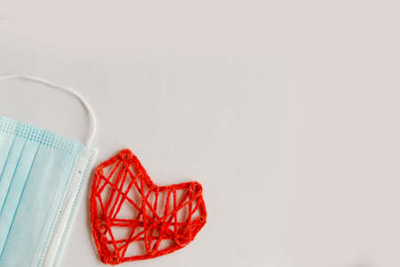 Red knitted heart and medical mask on white background. Valentine's Day during the coronavirus pandemic. Happy Valentine's Day 2021. Copy space for the textの写真素材